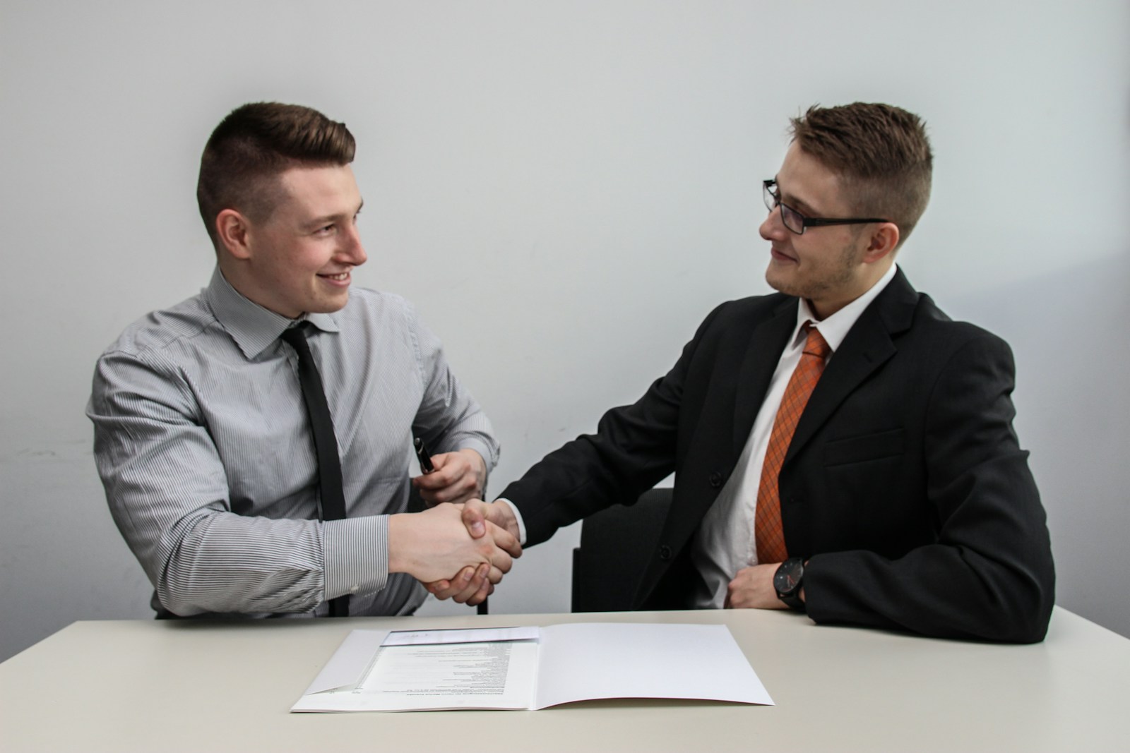 two men facing each other while shake hands and smiling, professional liability